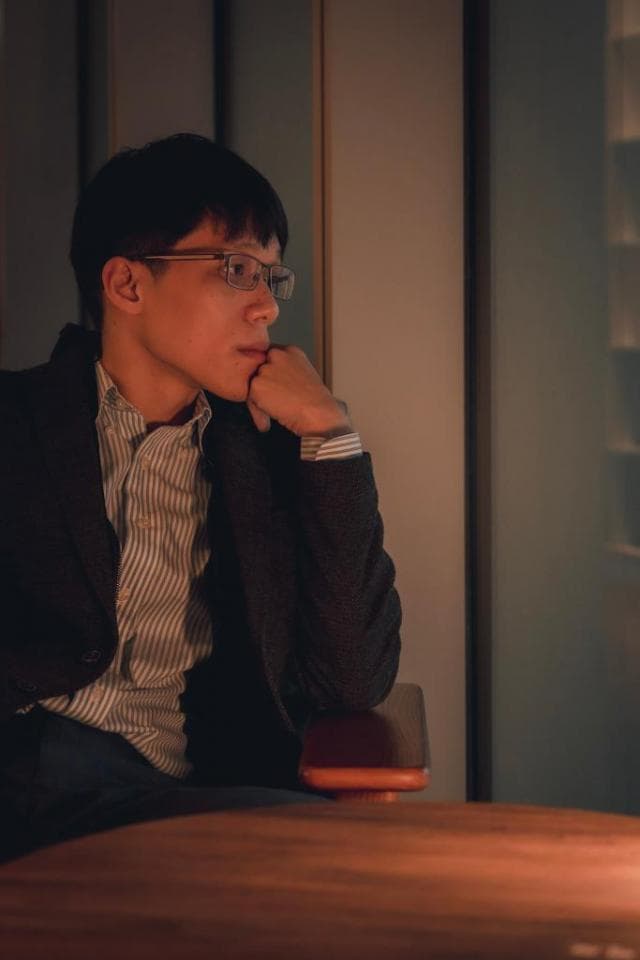 這張「一位戴眼鏡的年輕男子坐在椅子上,託著下巴沉思」的照片是。