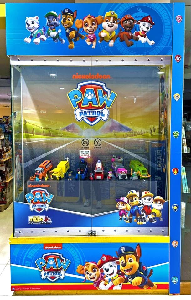 這張「汪汪隊立大功」的照片是一臺充滿童趣的遊戲機,機臺上有汪汪隊的角色圖案,以及汪汪隊的標誌。機臺的玻璃櫃裡擺放著汪汪隊的玩具車和人物模型,看起來非常可愛。