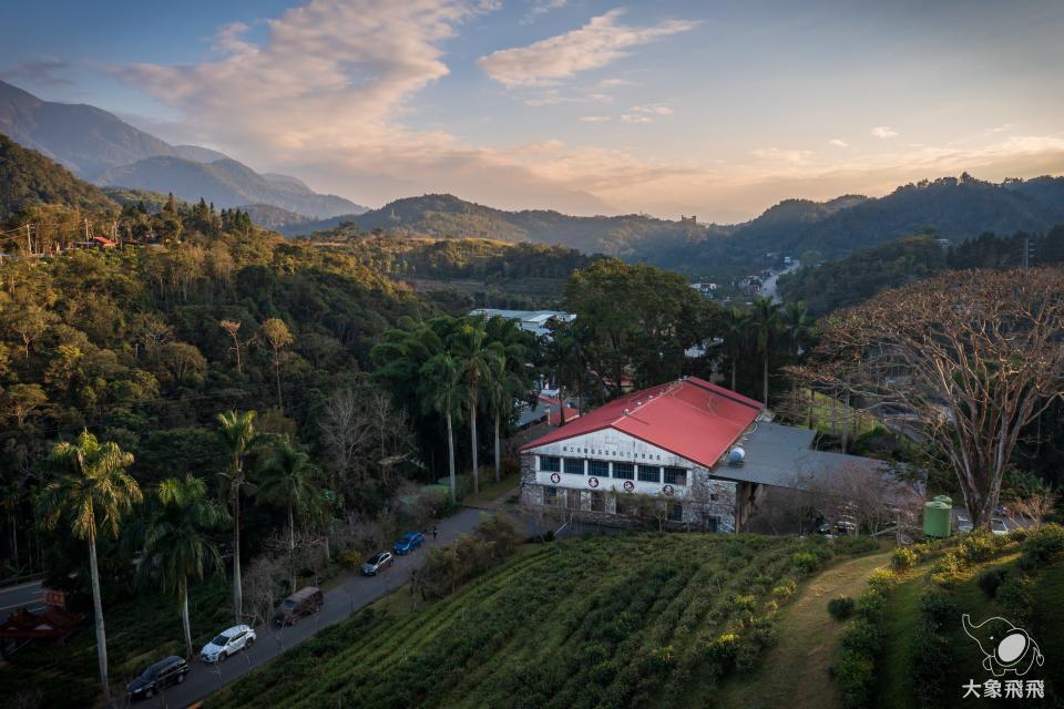 這張「山坡上的紅色屋頂建築」的照片是一座坐落在綠色山坡上的建築,建築物周圍種滿了樹木,可以看見屋頂上有許多窗戶。
