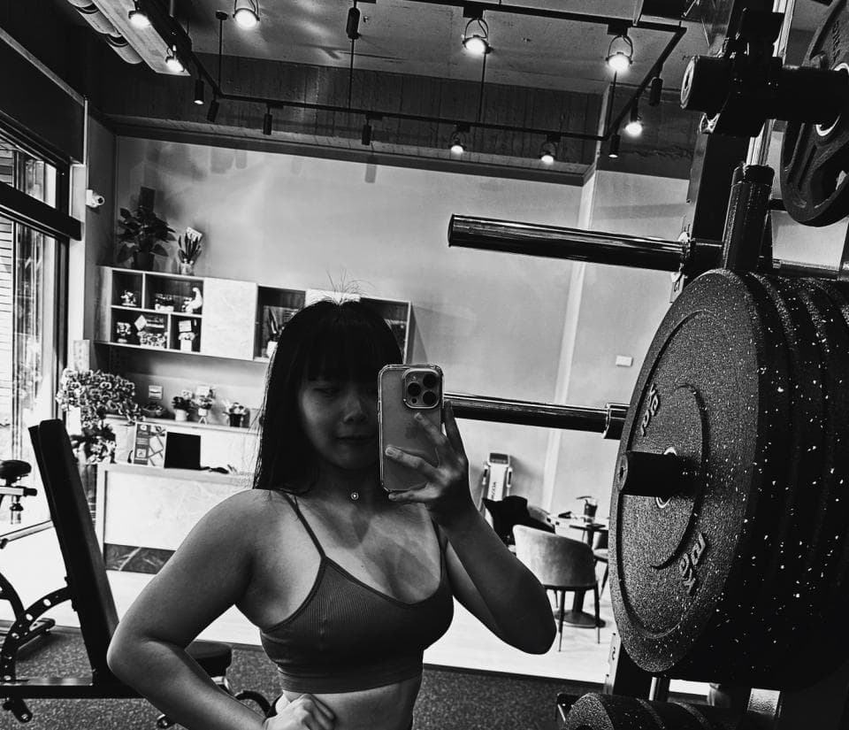 這張「健身房」的照片是一個年輕女性在健身房舉重的場景,她正在使用重量訓練器材,照片中可見她的肌肉線條和堅定的眼神,展現出積極運動的精神。