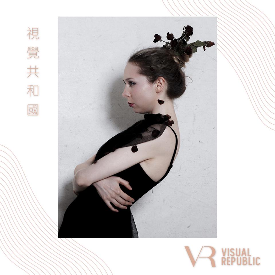 這張「」的照片是一名女性身穿黑色連衣裙,頭上戴著玫瑰花飾,在白色背景前擺姿勢。