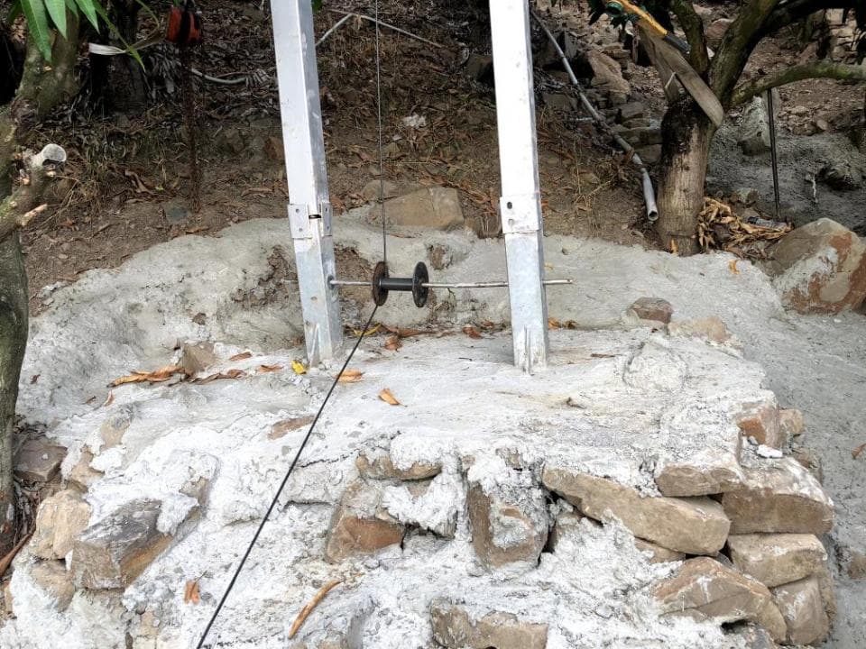 1) 照片顯示兩個水泥柱子固定在石頭地面上,柱子之間有一根鋼索連接,鋼索上有一個金屬滑輪