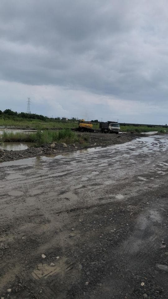 1) 照片顯示一條泥濘的道路,前方有兩輛車,一輛黃色的挖土機和一輛灰色卡車