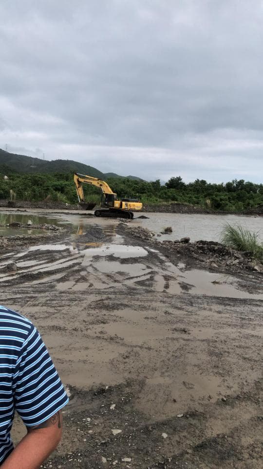 1) 照片顯示一輛黃色挖土機在一片泥濘的土地上,背景是綠色的山丘和灰色的天空