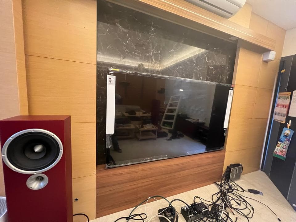 1) 照片顯示一個裝潢好的客廳,牆上掛著一台大型電視,電視下方有音響,地上有許多線材