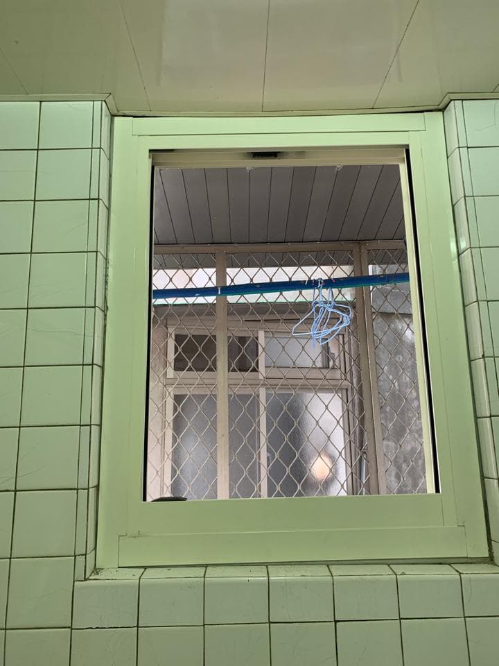 1. 照片顯示一個帶有綠色磁磚牆的浴室,浴室裡有一扇帶有格柵窗戶的窗戶