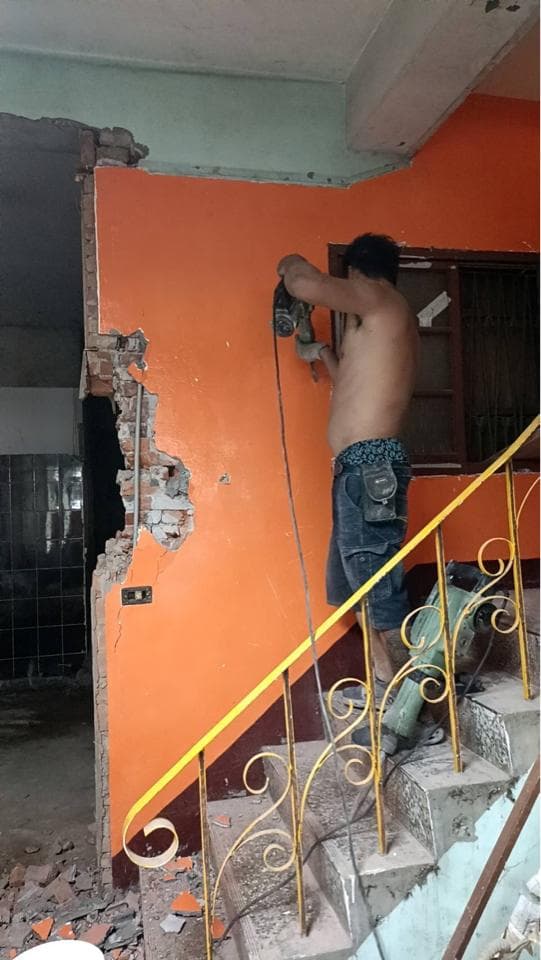 這張照片是一個工人正在用電鑽敲打牆壁。他站在樓梯上,用手握着電鑽,正在努力工作。