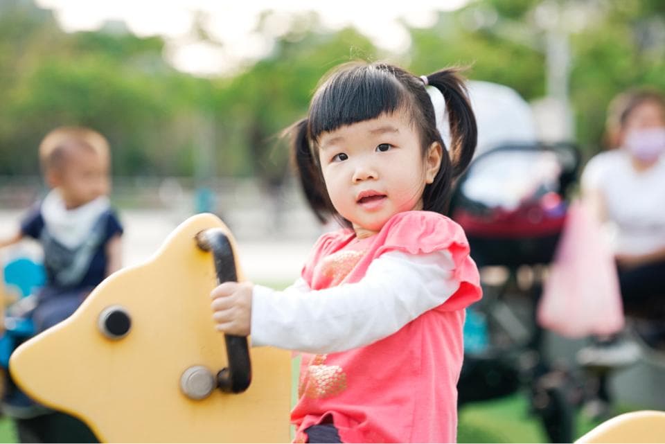 這張照片是一個可愛的小女孩在玩耍。她騎在一隻黃色的搖搖馬上,臉上洋溢著笑容,看起來非常開心。