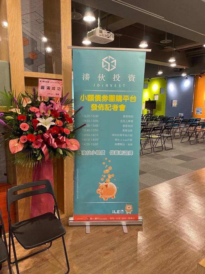 這張「投資說明會」的照片是一張宣傳海報,上面寫著「小額投資理財平臺 投資說明會」和一些投資資訊,旁邊放了一束鮮花和一張椅子。