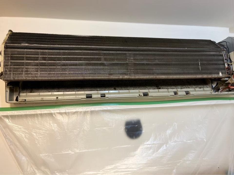 1) 照片顯示一個安裝在牆上的室內機冷氣機,冷氣機的濾網很髒,照片中還有塑膠布覆蓋著牆壁