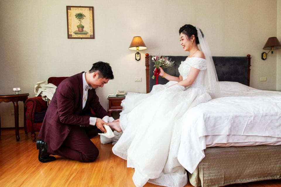 這張照片是一對新人在婚禮當天,新郎正在為新娘穿婚鞋。新郎跪在地上,專注地幫新娘穿鞋,新娘則微笑看著他,他們的眼神充滿了愛意和幸福。