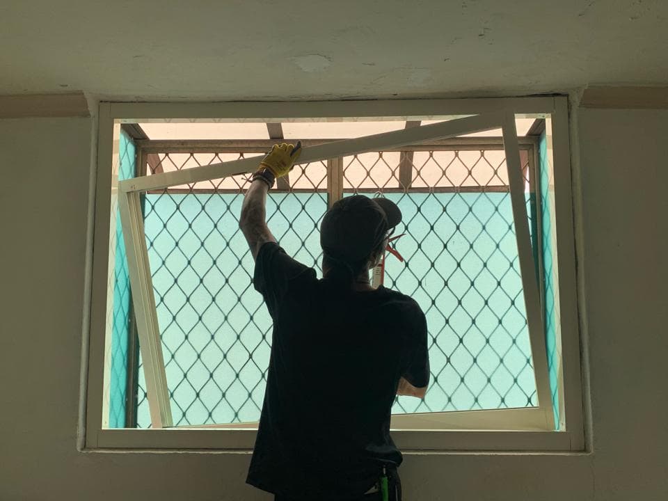 一個穿著黑色 T 恤和黃色手套的男人正在修理一個白色窗戶