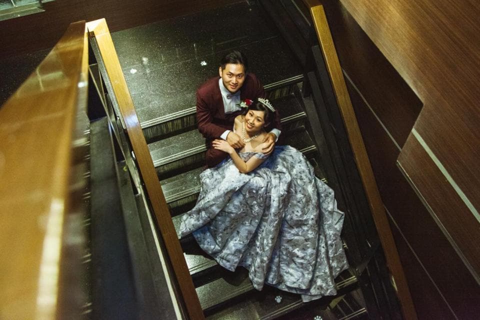 這張照片是一對新人在樓梯間拍婚紗照。新郎穿著深色的西裝,新娘穿著灰色的婚紗。他們互相依偎著,露出幸福的笑容。