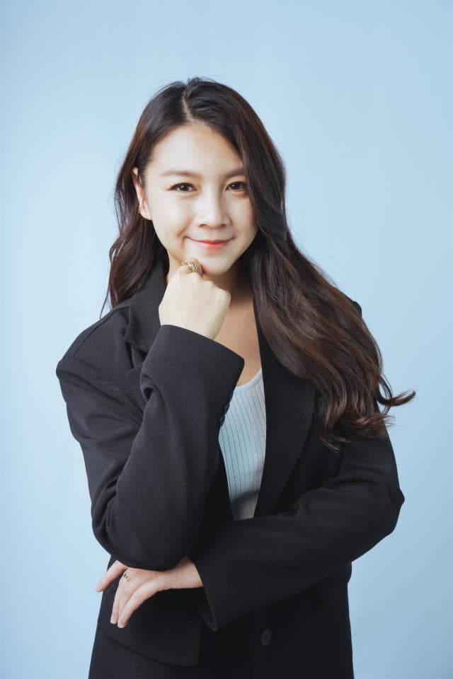 這張「年輕女性」的照片是,她穿著黑色西裝外套,一隻手放在下巴上,露出微笑的表情。