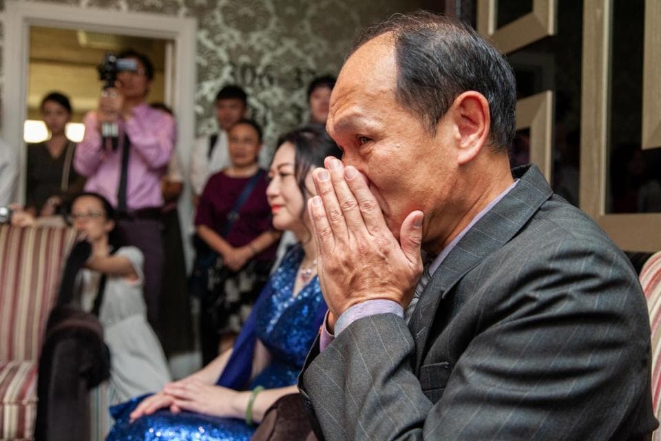 這張照片是一個男人在掩面哭泣,他站在許多人的中間,可能是參加一個婚禮或其他重要場合。他的臉上充滿悲傷,讓人感到心酸。他用手捂住臉,顯得非常難過。