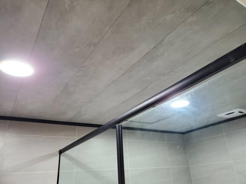 1) 照片顯示一個浴室的裝潢,天花板使用了水泥板,牆壁貼著白色瓷磚,看起來十分乾淨明亮