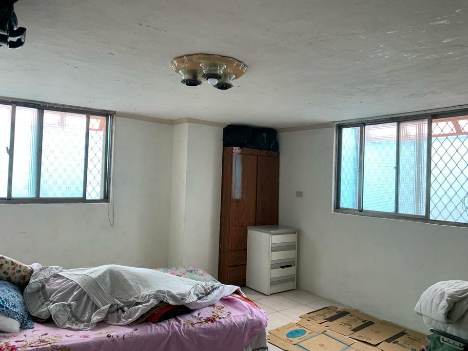 這張照片是一間臥室,最重要的部分是一張擺在房間中央的雙人床。床單是白色,上面有許多粉色和綠色的印花,床頭櫃上放着一個枕頭和一條毛毯。