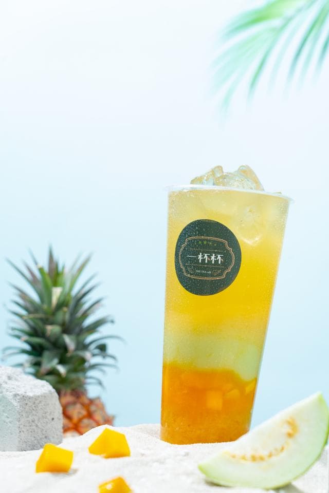 這張「水果茶」的照片是 一杯裝滿了水果和冰塊的飲料,旁邊有鳳梨、芒果和芭樂。