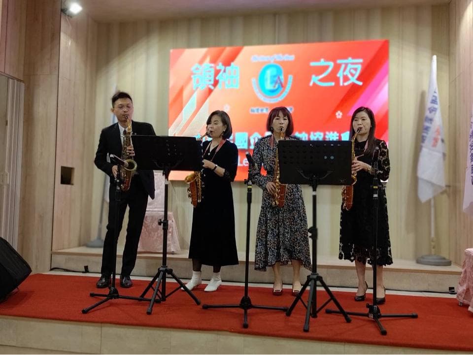 這張照片是四位音樂家正在演奏薩克斯風,背景是舞臺和紅色布幕。