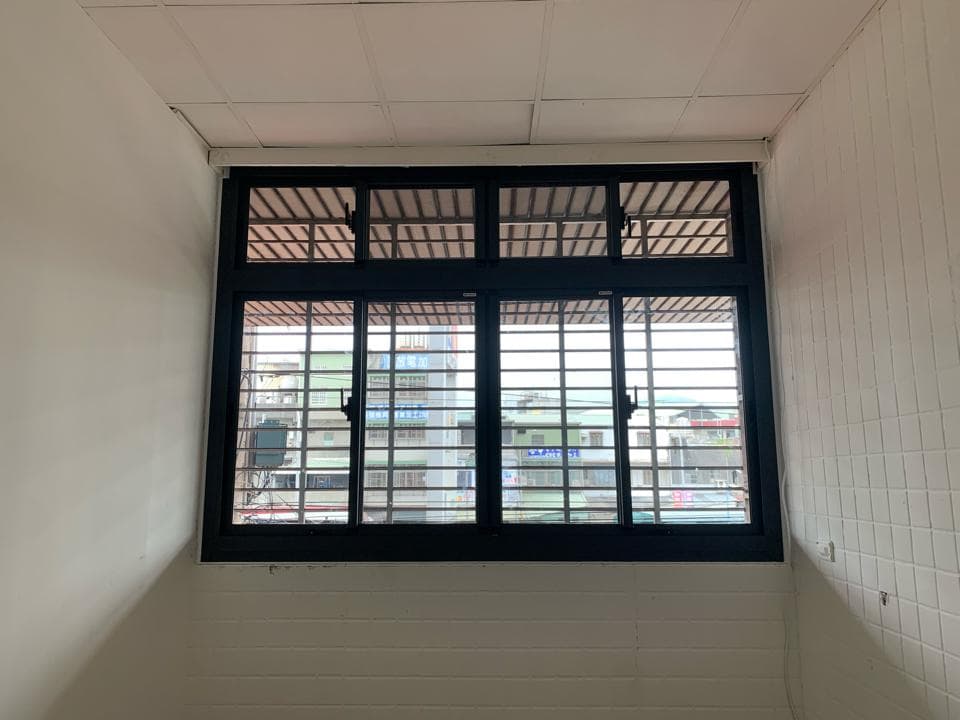 1) 照片中是一個有著黑色窗框的窗戶,窗戶上是鐵窗,窗戶外是白牆,可以看見窗戶的外部景觀