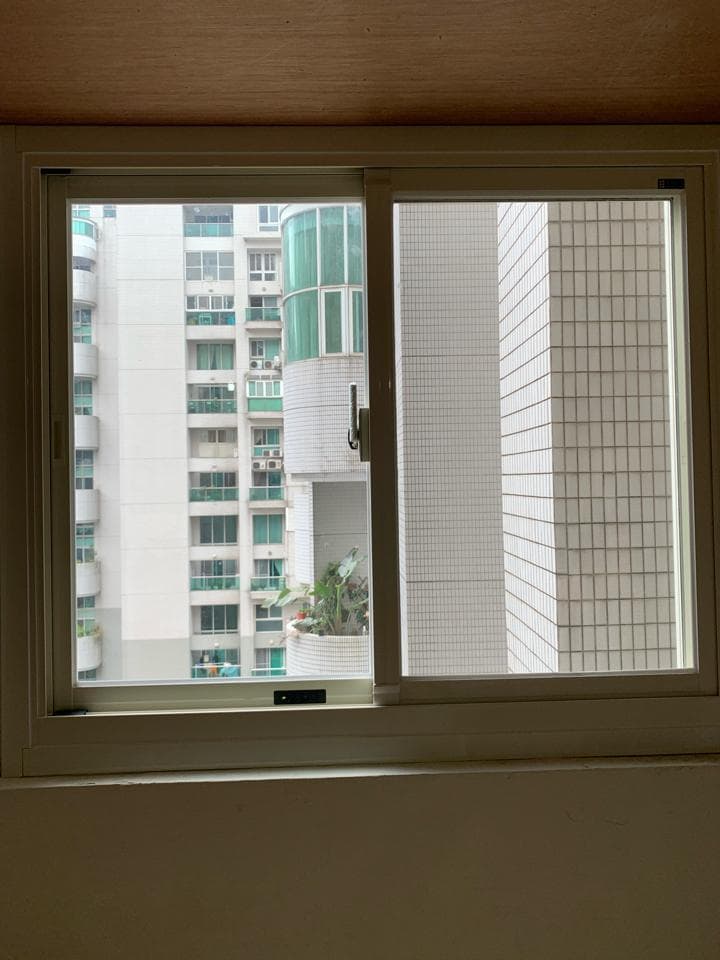 這張照片是一扇窗戶,窗戶外是一棟白色的高樓建築,建築物上有許多窗戶,窗戶旁有綠色的植物。