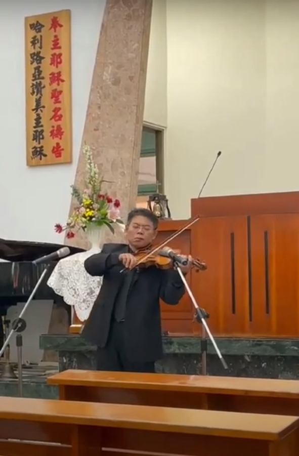 這張「一位男士在教堂演奏小提琴」的照片是,他穿著西裝,站在講臺前,演奏著小提琴。