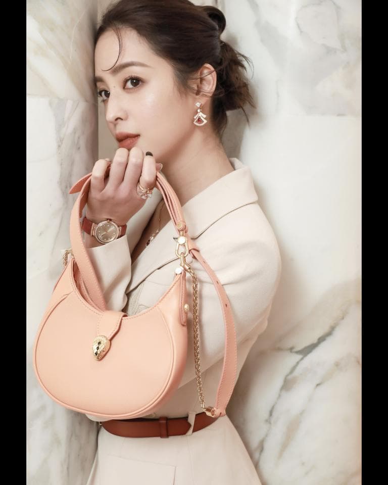 這張「時尚女性」的照片是一個穿著米色西裝外套的女子,她手上拿著一個粉紅色半月形包包,配戴著金色的手錶和耳環。