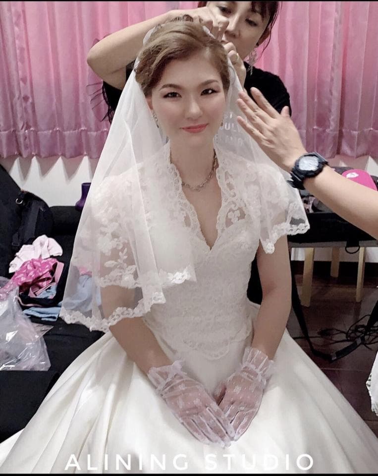 這張婚紗照是一個新娘正在穿婚紗的畫面,她戴著頭紗,並配戴著一雙白色蕾絲手套。