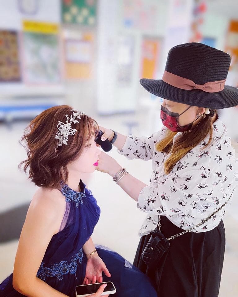 這張照片是一個正在化妝的女孩,她穿著一件藍色的禮服,頭上戴著一個精緻的頭飾。化妝師正在仔細地為她上妝,看起來很專注。