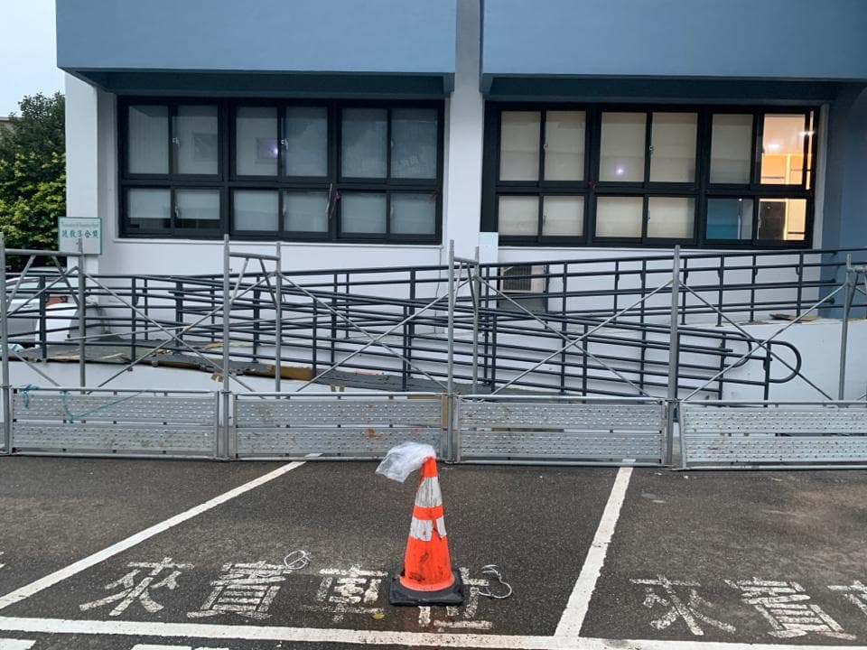 這張照片是建築工地的一部分,主要的部分是兩個金屬圍欄,圍欄中間有一個橙色的交通錐。