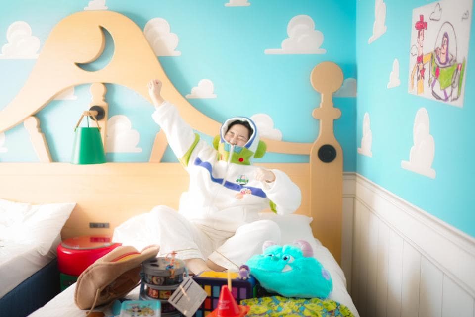 這張照片是一個以玩具總動員為主題的房間,房間裡有一個人穿著巴斯光年的服裝,坐在床上。