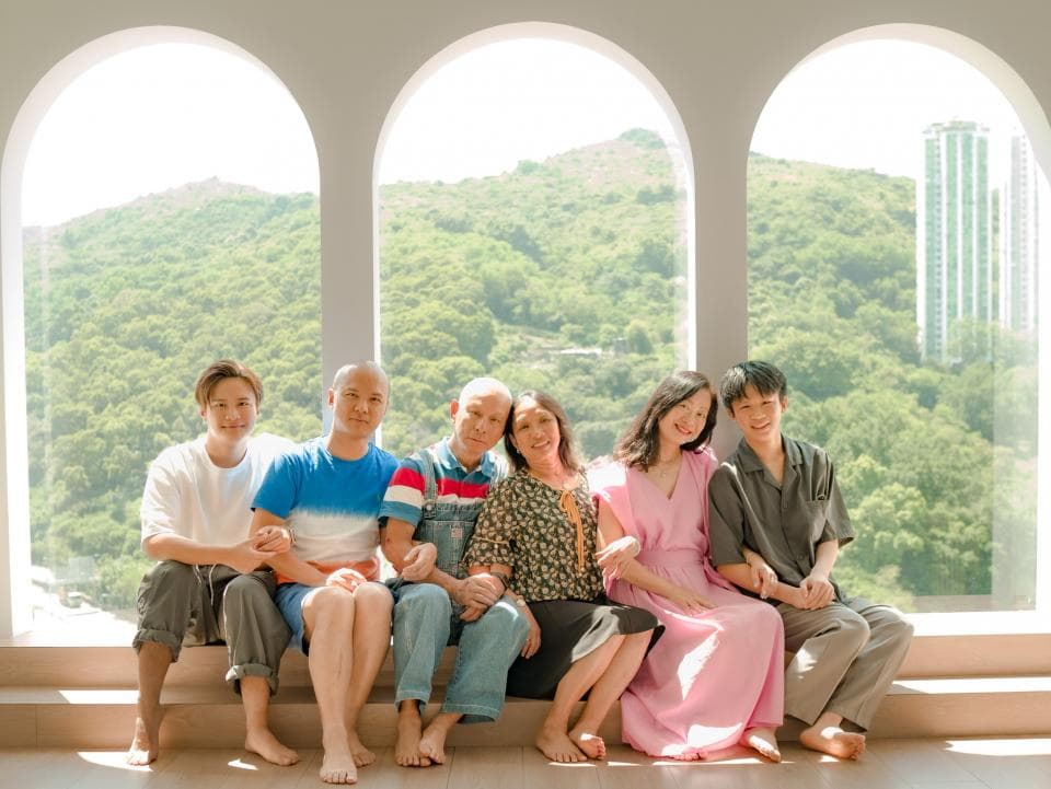 這張照片是一家人在一個陽光充足的房間裡,他們坐在窗邊,背景是風景如畫的山景。他們都面帶笑容,顯得非常開心和幸福。