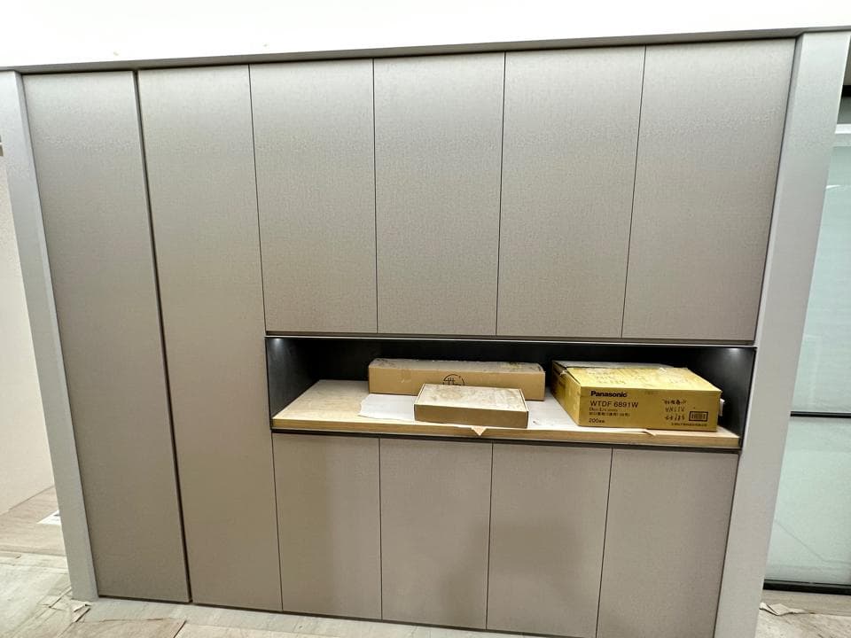 1) 照片顯示一個灰色的廚房櫥櫃,帶有四個門和一個架子,上面放着兩個紙箱