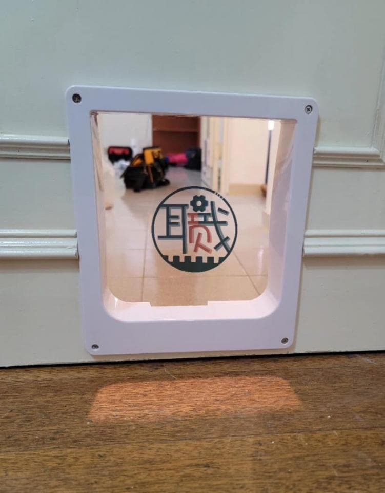 1) 照片顯示一個白色的貓門裝置,安裝在白牆上,貓門框中有一個透明玻璃窗,可以看到門內外的景色,地板是木地板