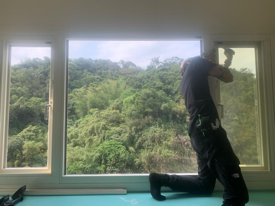 一個穿著黑色衣服的人正在裝修窗戶,窗戶外是綠色的樹木