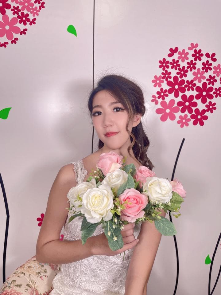 這張照片是一位穿著婚紗的女性,她手拿著一束粉紅和白色的玫瑰花束,花束中還有一些綠葉,看起來非常美麗。