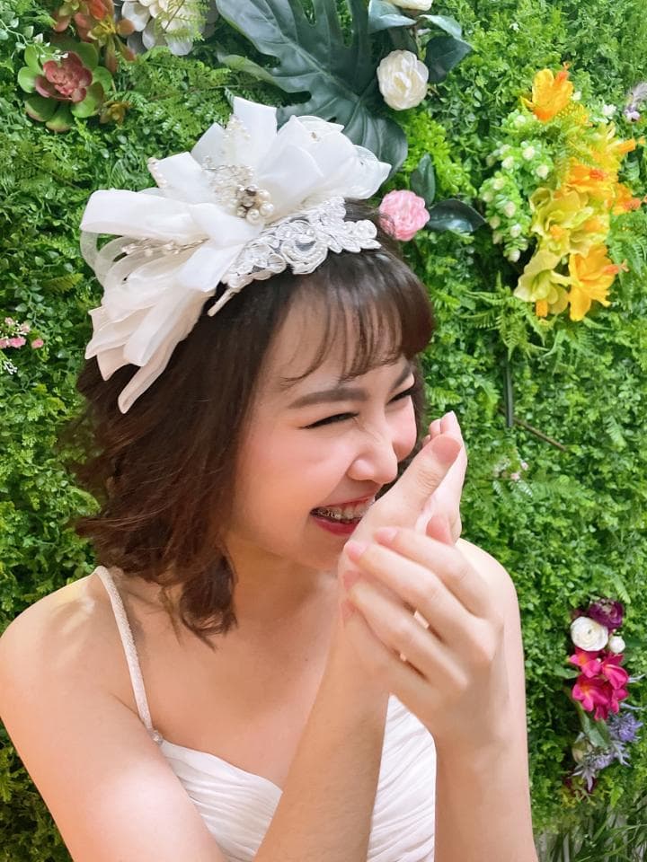 這張「一位戴著白色頭飾的女生,站在綠色背景前,開心地笑著」的照片是。