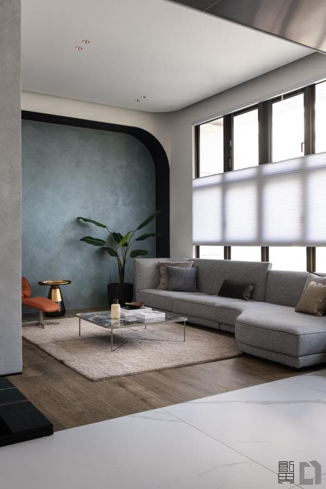 這張「客廳」的照片是一個現代化的客廳,有一個灰色沙發、一個咖啡桌和一盆綠色植物。房間裡的牆壁是淺藍色的,地板是木質的。