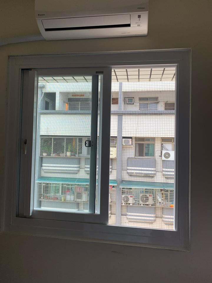 這張照片是一扇有著白色窗框的窗戶,窗戶外有防盜窗,可以看見外面是其他公寓。