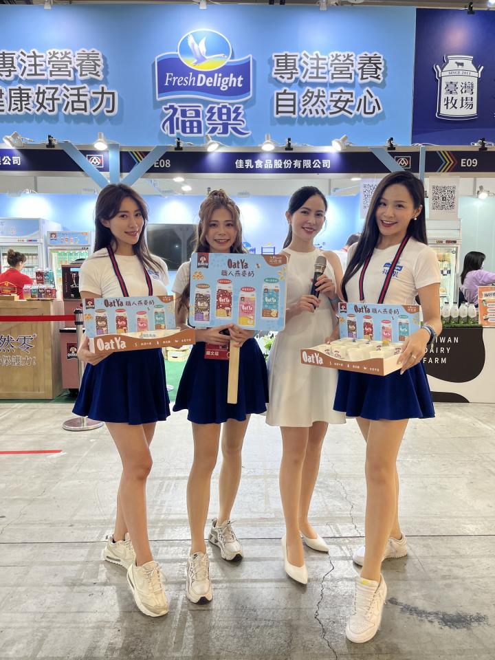 這張「四位女性在展覽攤位上宣傳產品」的照片是,她們穿著不同顏色的裙子,拿著產品的包裝盒,並面帶微笑地向鏡頭展示產品。