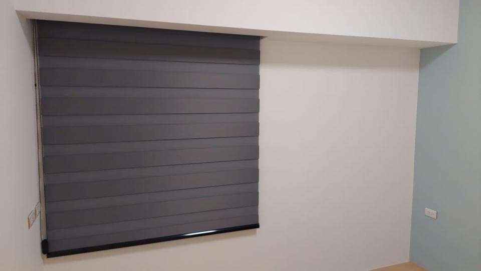 1) 照片中是一個灰色的窗簾,窗簾是降下來的狀態,窗簾下方是黑色的軌道,牆壁是白色的