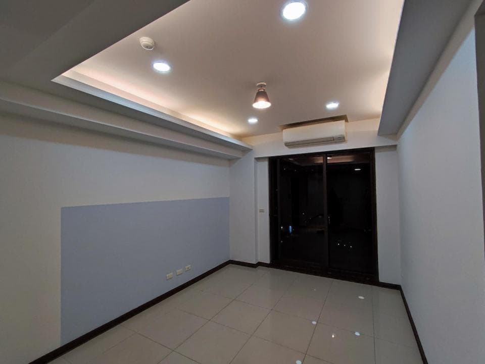 1) 照片顯示一個空蕩蕩的房間,房間的牆壁是白色和淺藍色的,地上是白色瓷磚,天花板上有嵌入式的燈光,房間中央有一扇黑色的推拉門