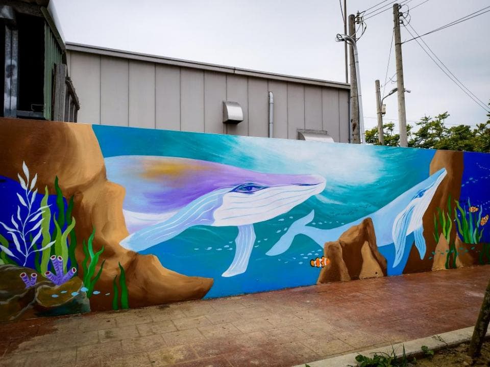 這張「牆壁上的鯨魚壁畫」的照片是一個藍色的背景,上面畫著兩隻鯨魚和一些珊瑚。