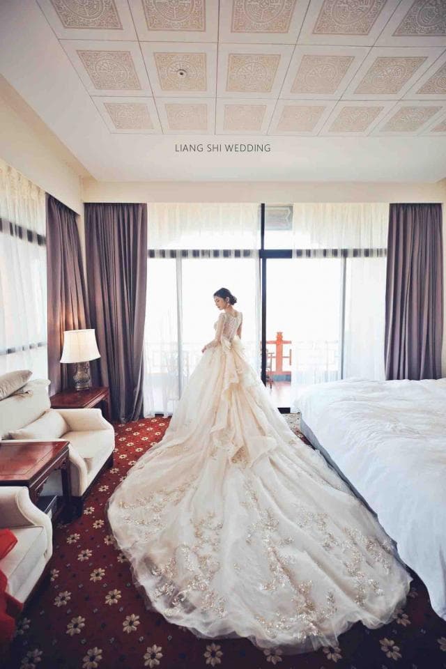 這張照片是一名身穿婚紗的新娘站在房間裡,她的婚紗非常漂亮,裙擺很長,幾乎鋪滿了整個房間。