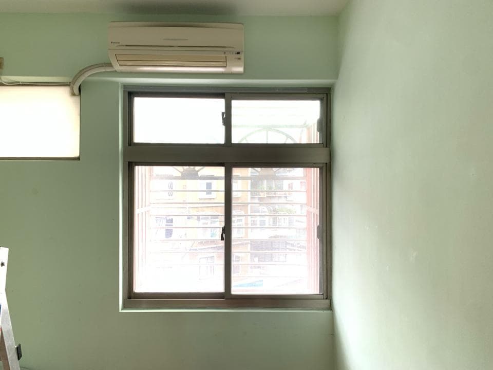 1) 照片顯示一個有綠色牆壁的房間,房間裡有一個窗戶,窗戶外可以看到建築物的模糊影像,房間裡的天花板上有一個空調