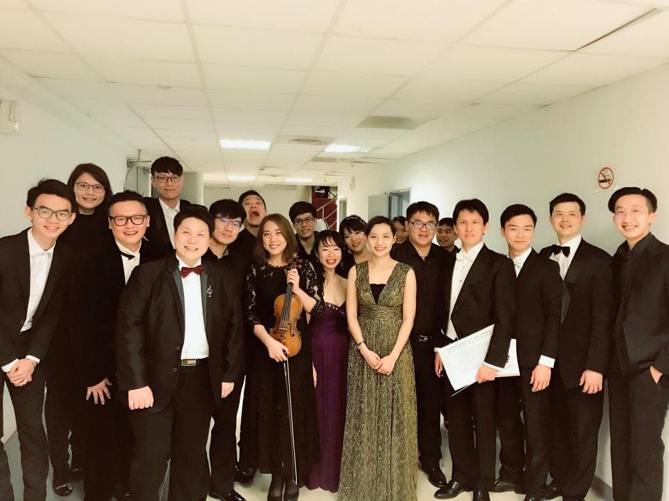 這張照片是一群穿著西裝的人在一個走廊里,他們看起来很开心的样子。照片的中心是一個穿著紫色礼服的女孩,她正在演奏小提琴。她旁边的女孩穿著一件绿色的长裙,看起來也很漂亮。