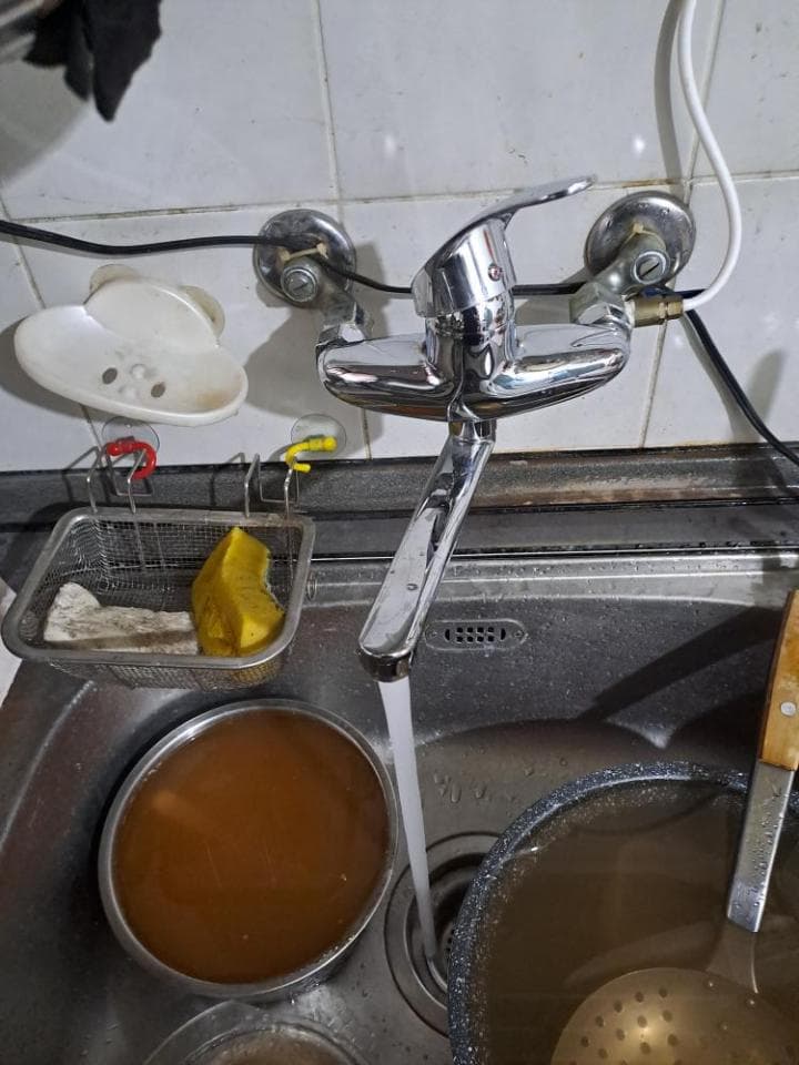 這張照片是一個廚房水槽,水槽裡有一個金屬水龍頭正在放水。水龍頭的下方是一個金屬水管,水正從水管裡流出來,流進水槽。水槽裡有一個金屬碗,碗裡裝滿了水。