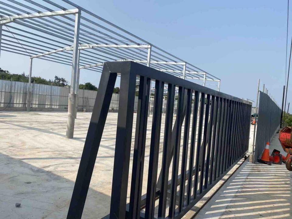 1) 照片顯示一個黑色金屬柵欄,柵欄位於水泥地上的建築物旁