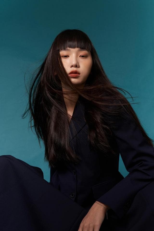 這張「年輕女性穿著黑色西裝外套,頭髮烏黑髮量豐厚,在藍色背景前擺著姿勢」的照片是。