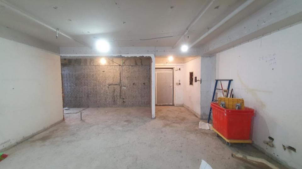 1) 照片顯示一個正在裝修的房間,牆壁尚未粉刷,地板上鋪設著水泥,房間裡有一個門通往另一個房間,以及一些裝修工具和一個紅色的工具箱